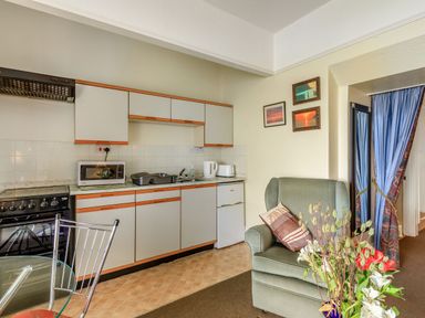 A kitchen with cabinets stove microwave kettle and toaster next to a green armchair and glass table with flowers at Clooneavin Apartment 4 in Lynmouth