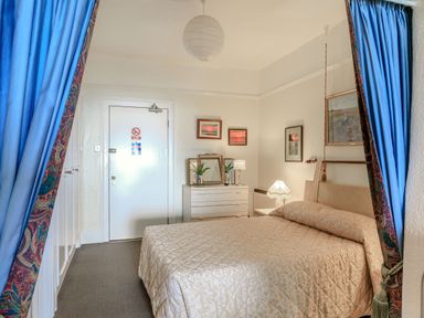 A bedroom with a bed bedside tables a dresser with lamps and plants and blue curtains at Clooneavin Apartment 4 in Lynmouth