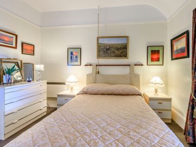 A bedroom with a bed and bedside tables with lamps and a dresser with pictures on Clooneavin Apartment 4 in Lynmouth