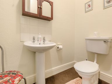 A bathroom with a pedestal sink a toilet a wall-mounted wooden cabinet and two framed pictures at Clooneavin Apartment 4 in Lynmouth