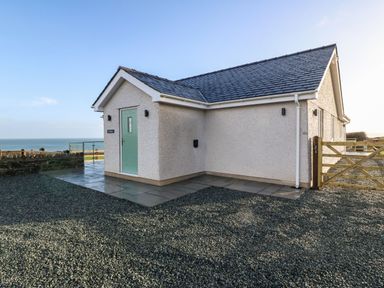 A single story house with a blue door and gravel driveway near the sea at Y Gorlan in Moelfre