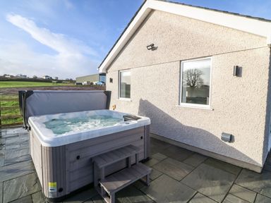 An outdoor hot tub with water and steps beside a house with two windows and stone tiles at Y Gorlan in Moelfre