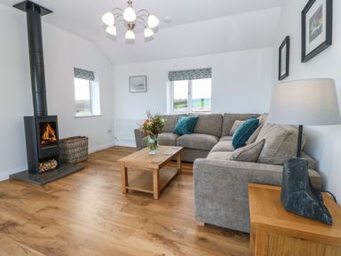 A living room with a sectional sofa table lamp wood burner and coffee table with flowers at Y Gorlan in Moelfre