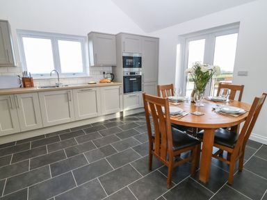A kitchen with grey cabinets a wooden dining table set for four with flowers in a vase at Y Gorlan in Moelfre