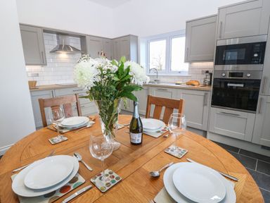 A kitchen with a round wooden dining table set with plates wine glasses and cutlery and flowers on the table at Y Gorlan in Moelfre
