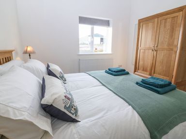 A bedroom with a double bed with pillows and folded towels near a window and a wooden wardrobe at Y Gorlan in Moelfre