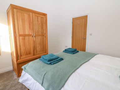 A bedroom with a wooden wardrobe a wooden door and a bed with green blankets and folded towels at Y Gorlan in Moelfre