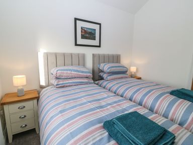 A bedroom with two single beds with striped bedding two bedside tables with lamps and a framed picture on the wall at Y Gorlan in Moelfre