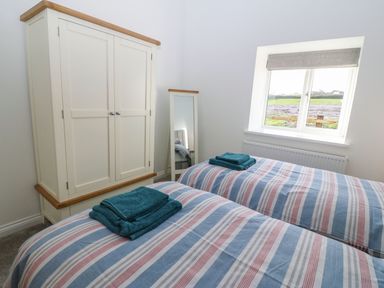 A bedroom with two single beds with striped bedding a white wardrobe a standing mirror and a window at Y Gorlan in Moelfre