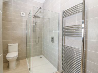 A bathroom with a toilet a glass shower enclosure and a chrome heated towel rail at Y Gorlan in Moelfre