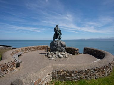A statue on a stone platform with a curved stone wall overlooking the sea at Y Gorlan in Moelfre