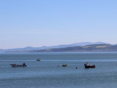 A sea with boats floating on water and hills in the background at Y Gorlan in Moelfre
