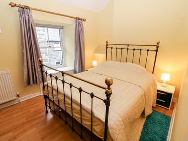 A bedroom with a metal bed frame a bed with a beige quilt and two bedside tables with lamps at Gerlan in Harlech