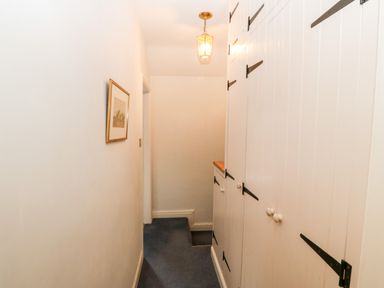 A narrow hallway with white paneled cupboards and a blue carpet at Gerlan in Harlech