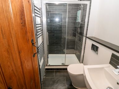 A bathroom with a wooden door a white toilet a white sink and a glass shower enclosure with black tiled walls at Gerlan in Harlech