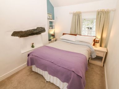 A bedroom with a bed covered with a purple blanket and bedside tables with lamps at Gerlan in Harlech