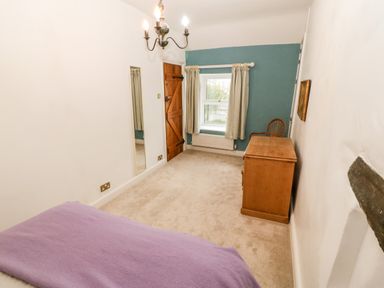 A bedroom with a wooden desk and chair a bed with a purple blanket a window with curtains and a wooden door at Gerlan in Harlech