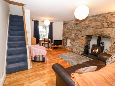 A living room with a stone fireplace a wood stove a brown leather sofa a blue carpeted stairway and a small wooden desk at Gerlan in Harlech