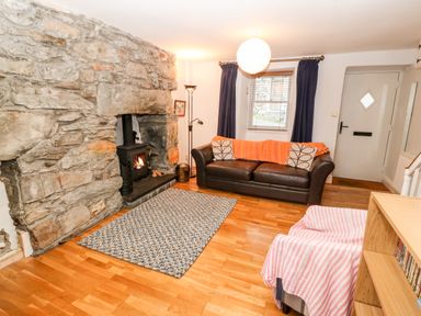 A living room with a stone fireplace a wood stove a brown sofa with cushions a patterned rug and a pink striped chair at Gerlan in Harlech