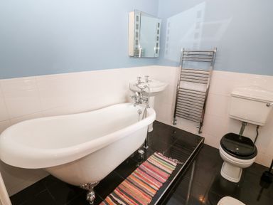 A bathroom with a white clawfoot bathtub a pedestal sink a wall-mounted mirror a heated towel rail and a toilet with a black seat at Gerlan in Harlech