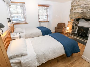 A bedroom with two single beds blue blankets a stone fireplace an armchair and wooden flooring at Gerlan in Harlech