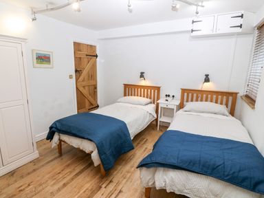 A bedroom with two single beds a blue blanket a white nightstand and a wooden door at Gerlan in Harlech