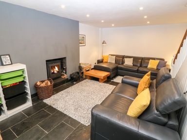 A living room with a black leather sofa set a wooden coffee table a fireplace with fire a gray wall and storage bins at Gerlan in Harlech