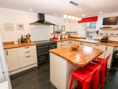 A kitchen with wooden countertops a cooking stove a kitchen island with a bowl of fruit and red stools at Gerlan in Harlech