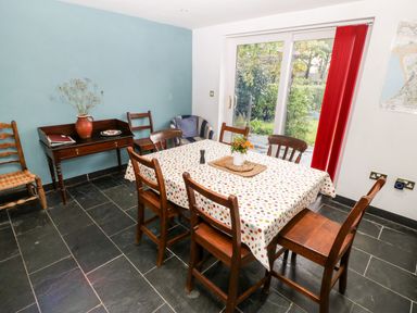 A dining room with a table covered with a polka dot tablecloth and six wooden chairs by sliding glass doors at Gerlan in Harlech