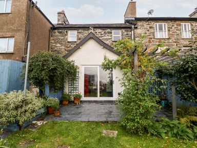 A garden patio with potted plants and green vegetation outside a stone house with sliding glass doors at Gerlan in Harlech