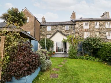 A backyard garden with grass stone path plants and a stone house with a small porch at Gerlan in Harlech