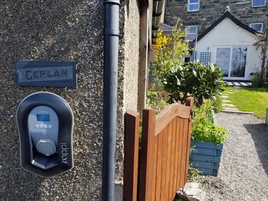 An outdoor view of a pathway leading to a house with garden plants and a wooden gate at Gerlan in Harlech