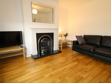 A living room with a black leather sofa a fireplace a mirror flowers on a table and a television on a stand at Gatehouse in Moville County Donegal
