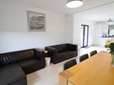 A living area with two black leather sofas a wooden dining table with chairs and a kitchen in the background at Gatehouse in Moville County Donegal