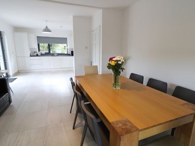 A dining area with a wooden table and chairs next to a kitchen with white cabinets and a window at Gatehouse in Moville County Donegal