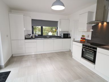 A kitchen with white cabinets a window with grey blind a microwave toaster kettle fruit stand and oven at Gatehouse in Moville County Donegal