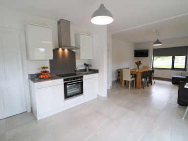 A kitchen area with white cabinets a stove and an oven a dining table with chairs and a TV on the wall at Gatehouse Moville County Donegal