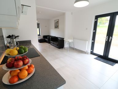 A kitchen with a tiered fruit tray on the counter and a living area with black sofas and a high chair at Gatehouse in Moville County Donegal
