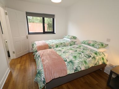 A bedroom with two single beds with leafy printed bedding and pink throws near a window at Gatehouse in Moville County Donegal