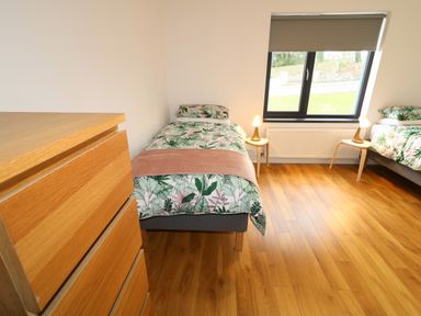 A bedroom with two single beds floral bedding wooden floor a window and a wooden chest of drawers at Gatehouse in Moville County Donegal