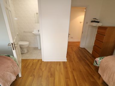 A bedroom with wooden floor two single beds a wooden chest of drawers and a bathroom with tiled walls at Gatehouse in Moville County Donegal