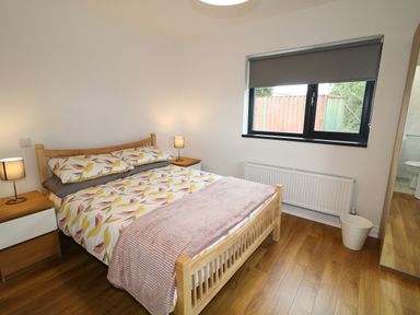 A bedroom with a wooden bed with patterned bedding two bedside tables with lamps a window with grey blinds and a mirror reflecting a bathroom at Gatehouse Moville County Donegal