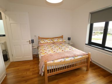 A bedroom with a wooden bed with patterned bedding two bedside tables with lamps a window with a roller blind and an open door to a bathroom at Gatehouse in Moville County Donegal