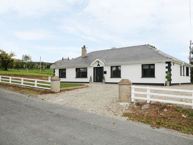 A single story white house with grey roof and black windows with gravel driveway and white fence at Gatehouse in Moville County Donegal