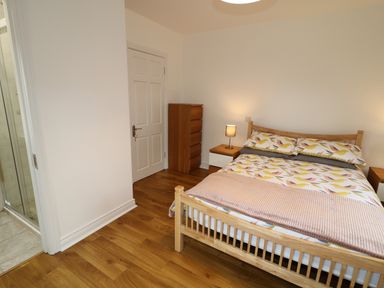A bedroom with a wooden bed a bedside table with a lamp a chest of drawers and a door leading to a bathroom at Gatehouse in Moville County Donegal