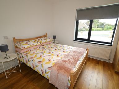 A bedroom with a wooden bed frame, bedside tables with lamps, window with roller blind, and wooden floor at Gatehouse in Moville County Donegal