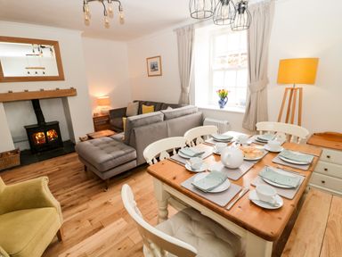A dining table set with cups plates and a teapot next to a living room with a fireplace sofa and armchair at Curlew Cottage 2 Fenkle Street Holy Island