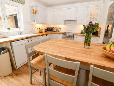 A kitchen with wooden countertops a wooden island with chairs a vase of flowers and a bowl of fruit at Curlew Cottage 2 Fenkle Street Holy Island
