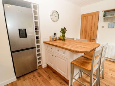 A kitchen area with a stainless steel refrigerator a wooden countertop with flowers a bowl of fruit and chairs at Curlew Cottage 2 Fenkle Street Holy Island
