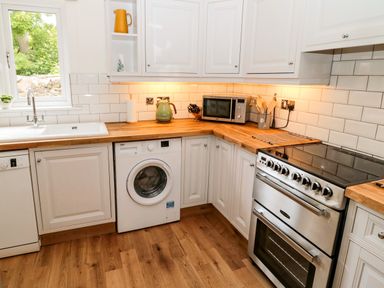 A kitchen with white cabinets wooden countertop a washing machine silver stove and microwave at Curlew Cottage 2 Fenkle Street Holy Island